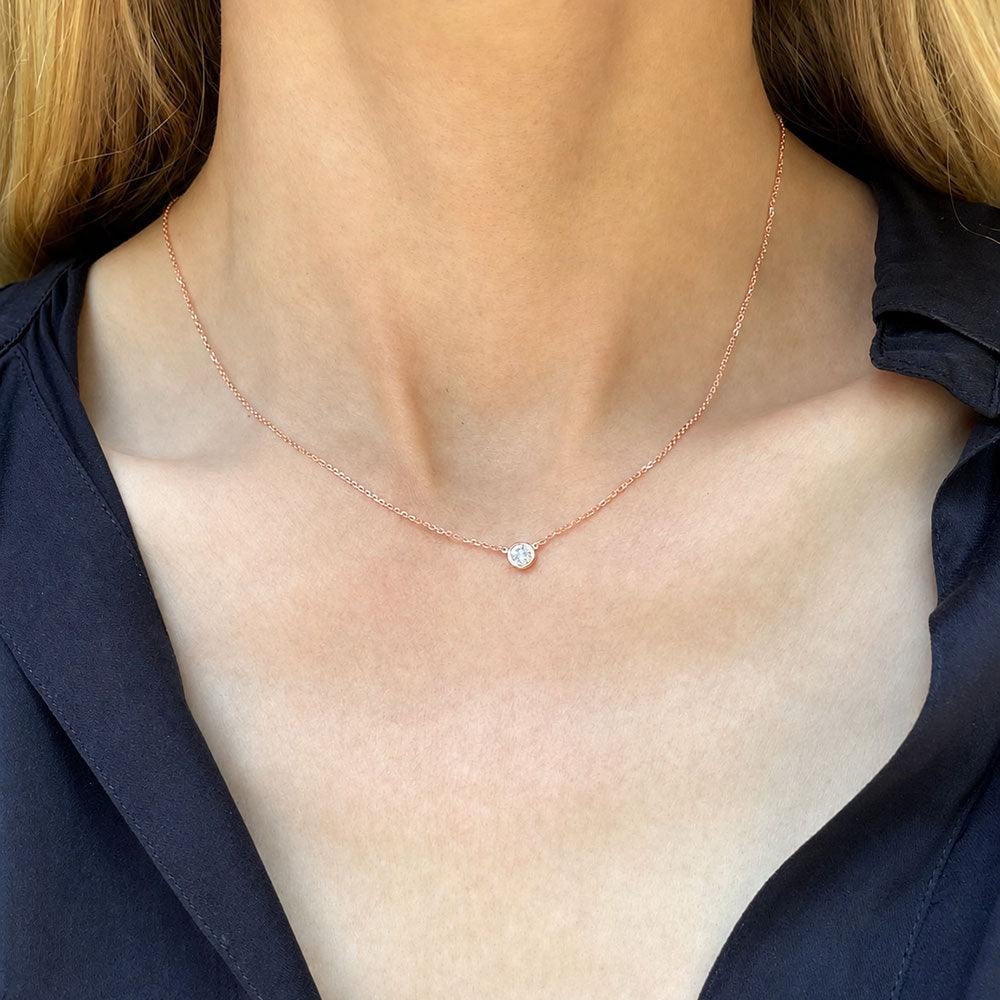 Necklace with a small round bezel set diamond pendant on a person wearing a dark blue top.
