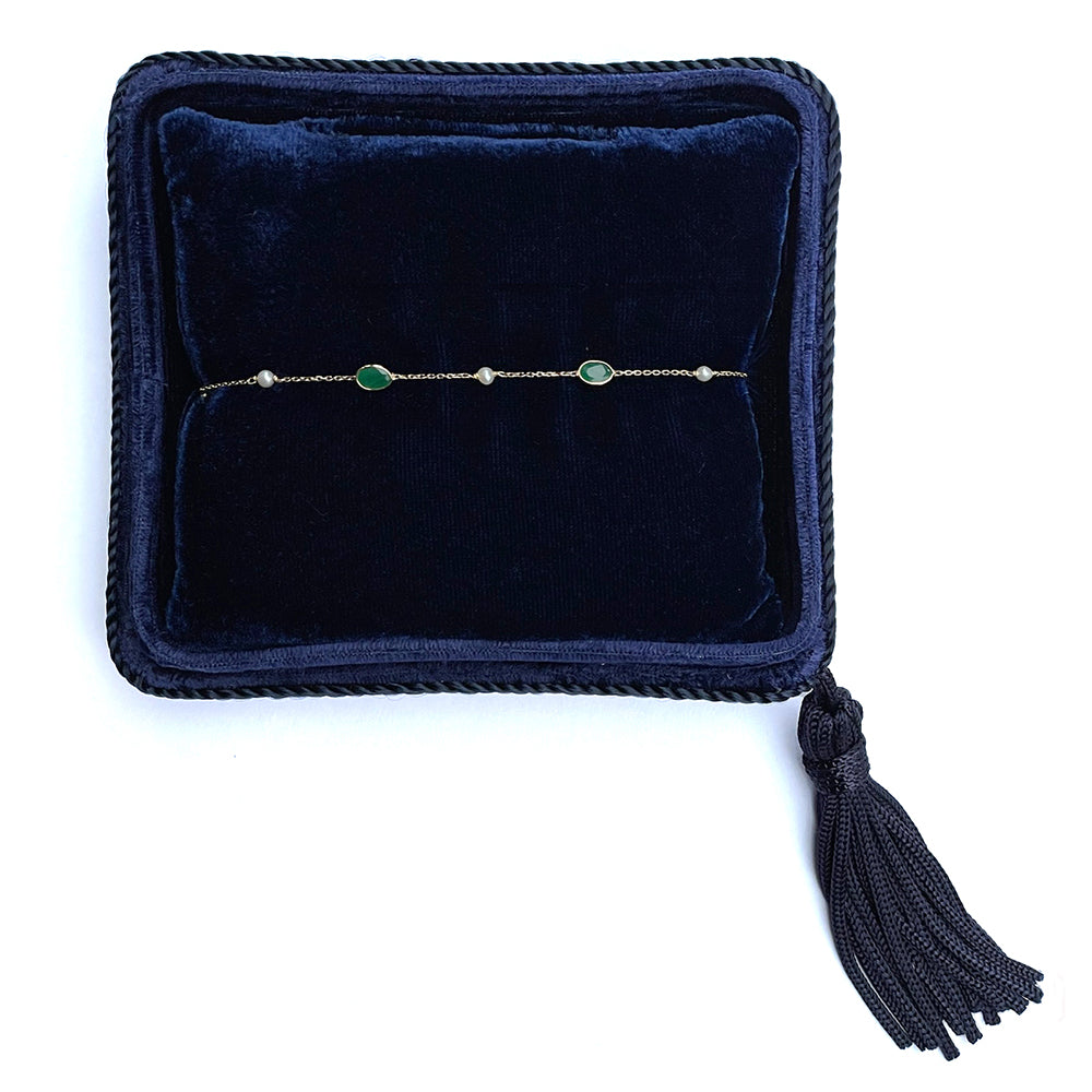 Bracelet with green stones on a dark blue velvet pillow with tassel