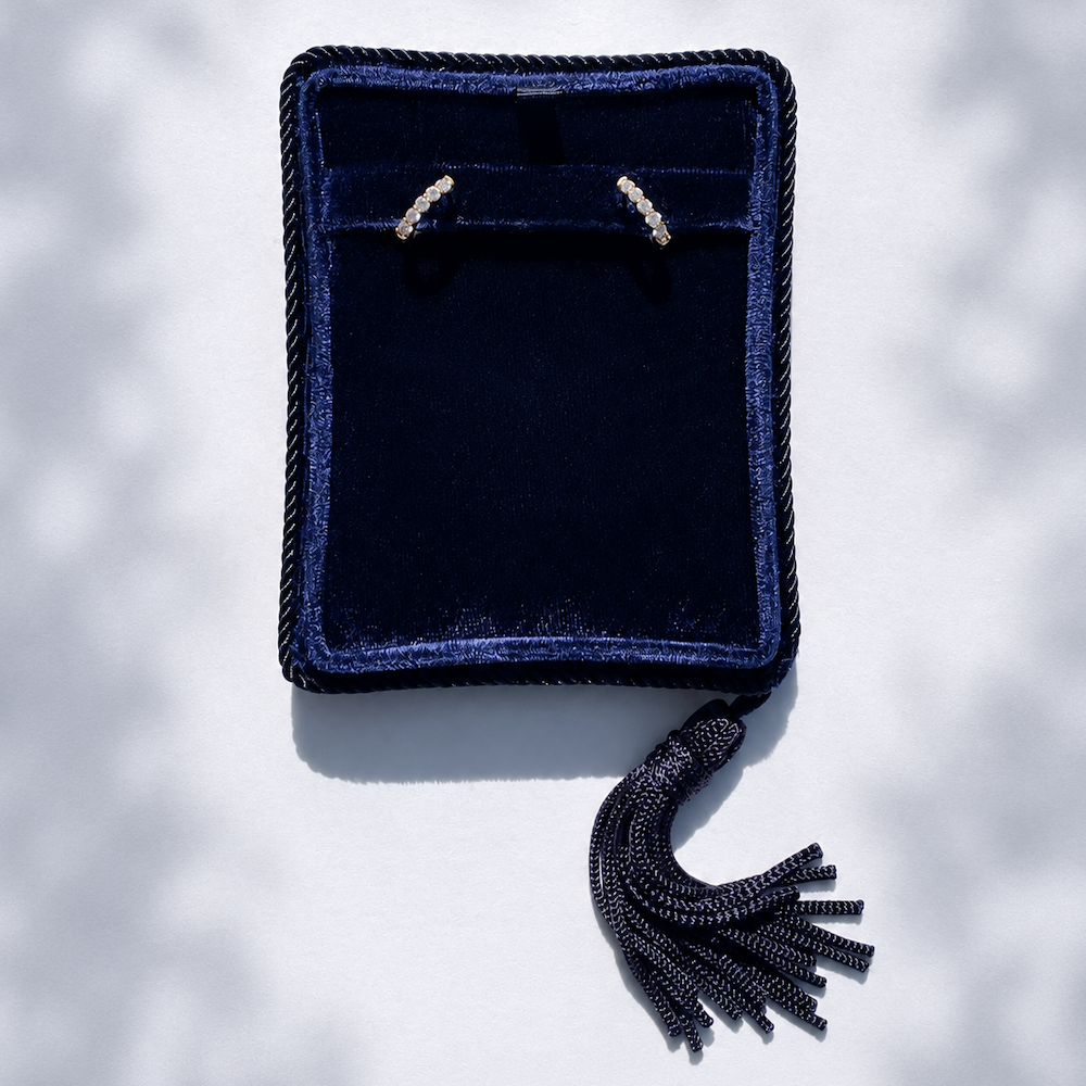 Diamond huggie hoop earrings in a navy blue velvet jewelry box with tassel on a white background