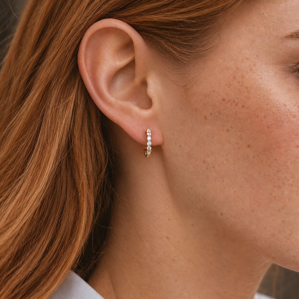 Close-up of a model wearing yellow gold diamond huggie hoop earrings.