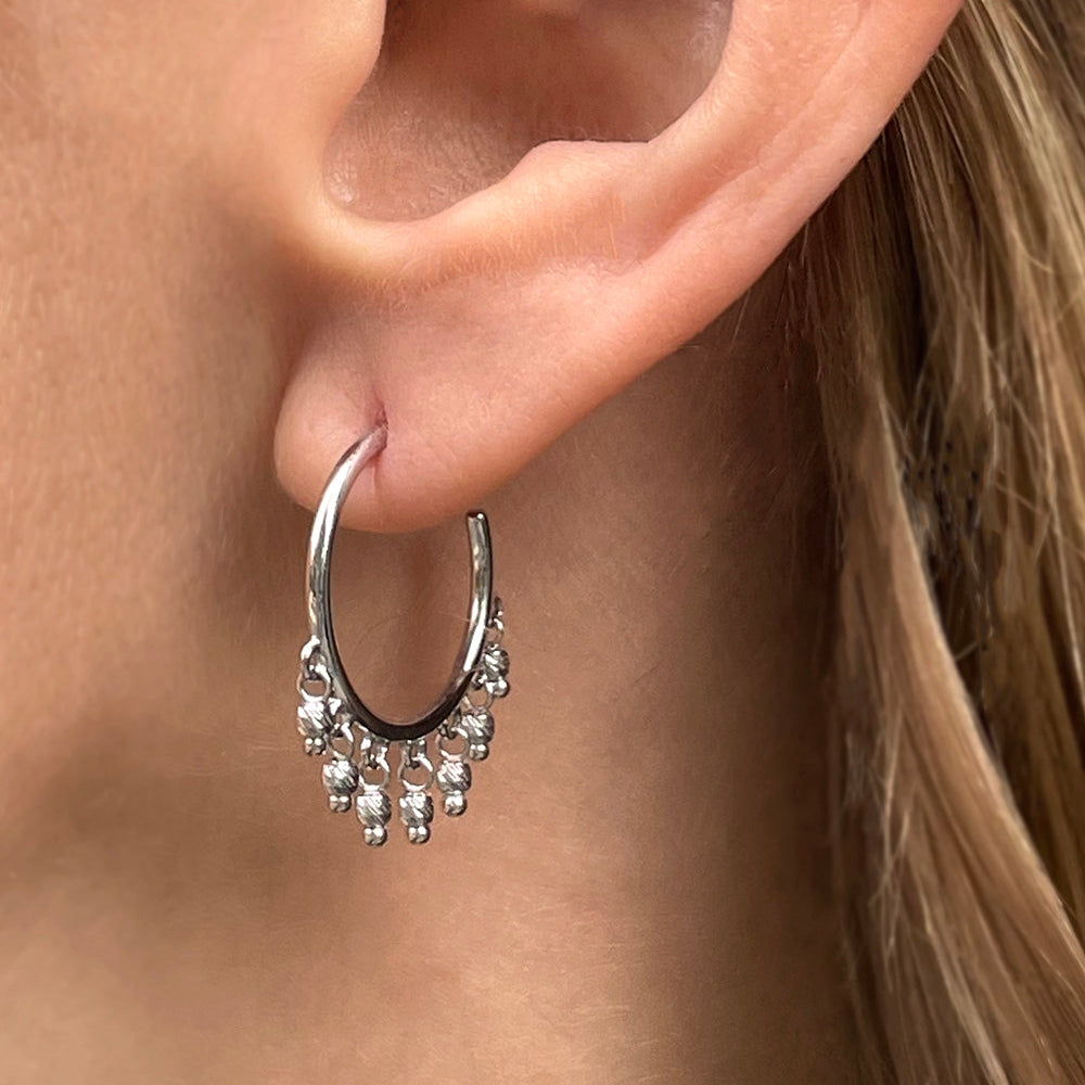 14K White Gold open hoop beaded earrings with dangling diamond-cut bead accents on a models ear