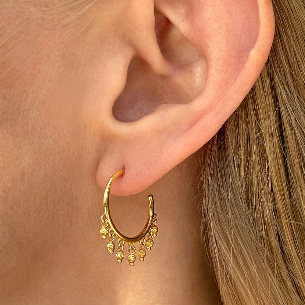 14K Yellow Gold open hoop beaded earrings with dangling diamond-cut bead accents on a models ear