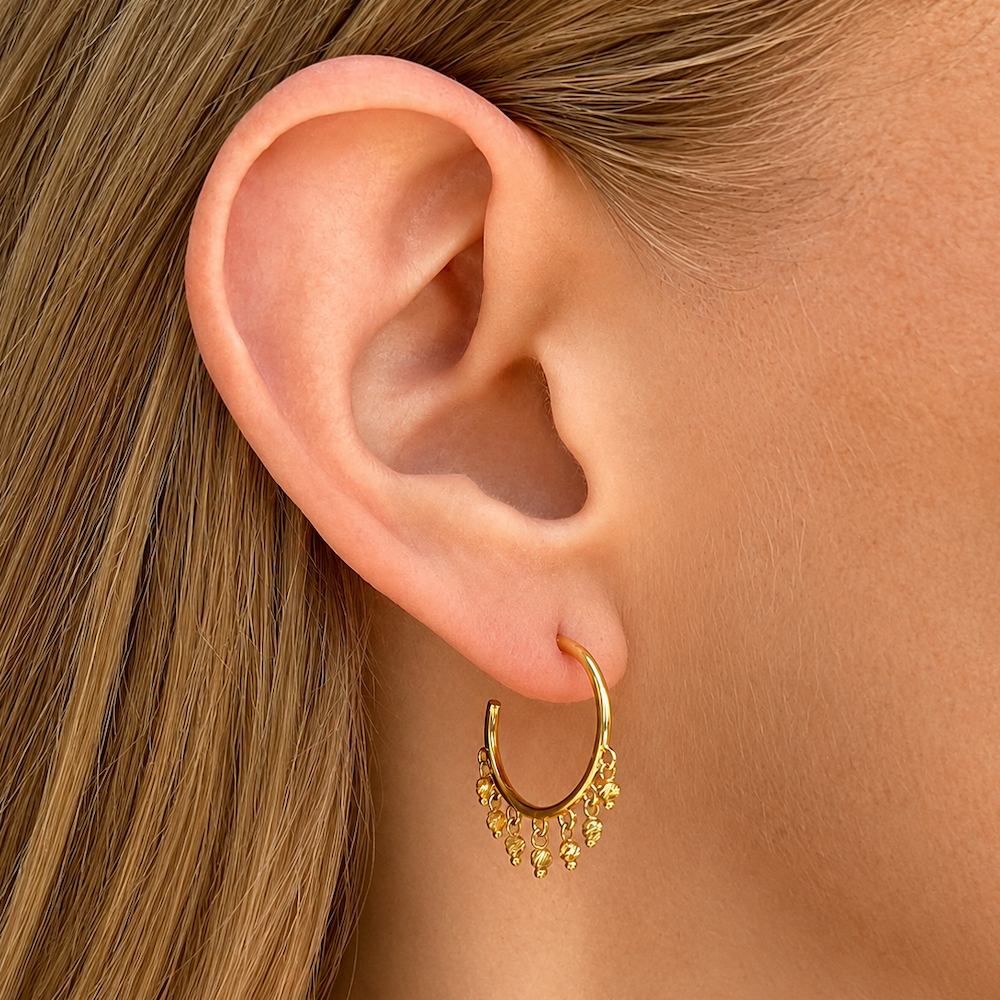 14K Yellow Gold open hoop beaded earrings with dangling diamond-cut bead accents on a models ear