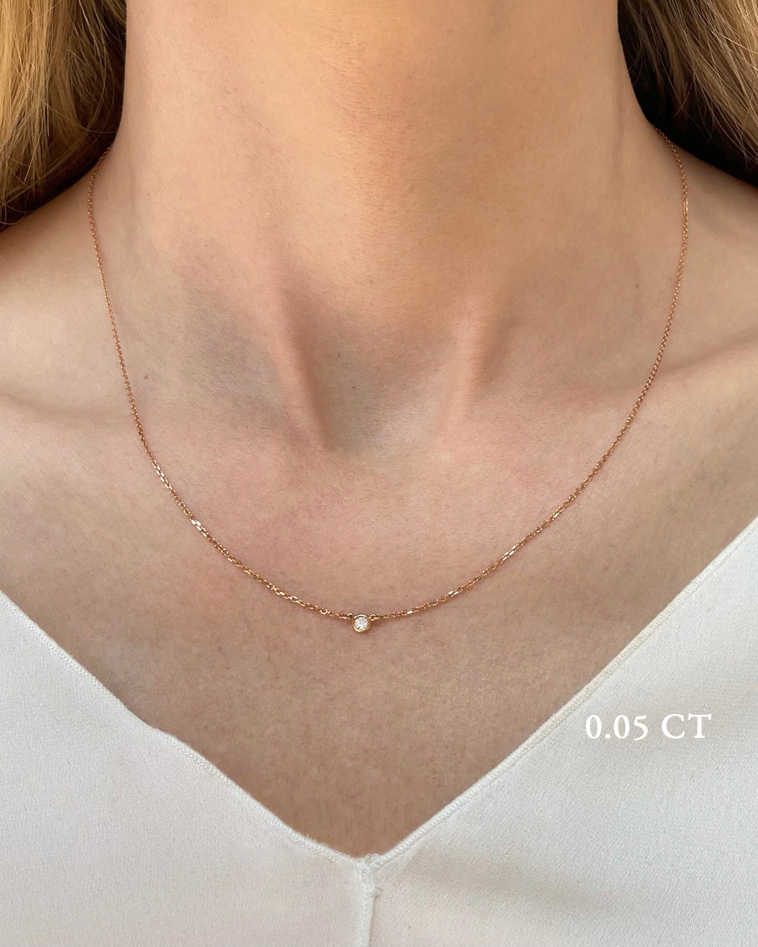 A delicate rose gold necklace with a 0.05 carat diamond, bezel set, shown on a model's neck. 