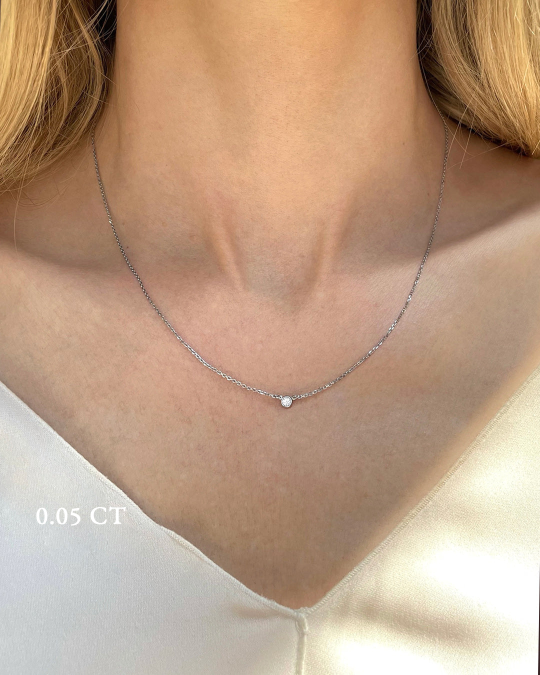 A delicate white gold necklace with a 0.05 carat diamond, bezel set, shown on a model's neck. 