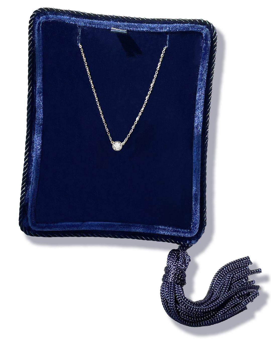 A delicate 14k white gold chain necklace with a 0.15 carat round brilliant-cut diamond bezel set pendant, displayed inside a dark navy velvet jewelry box with a tassel.