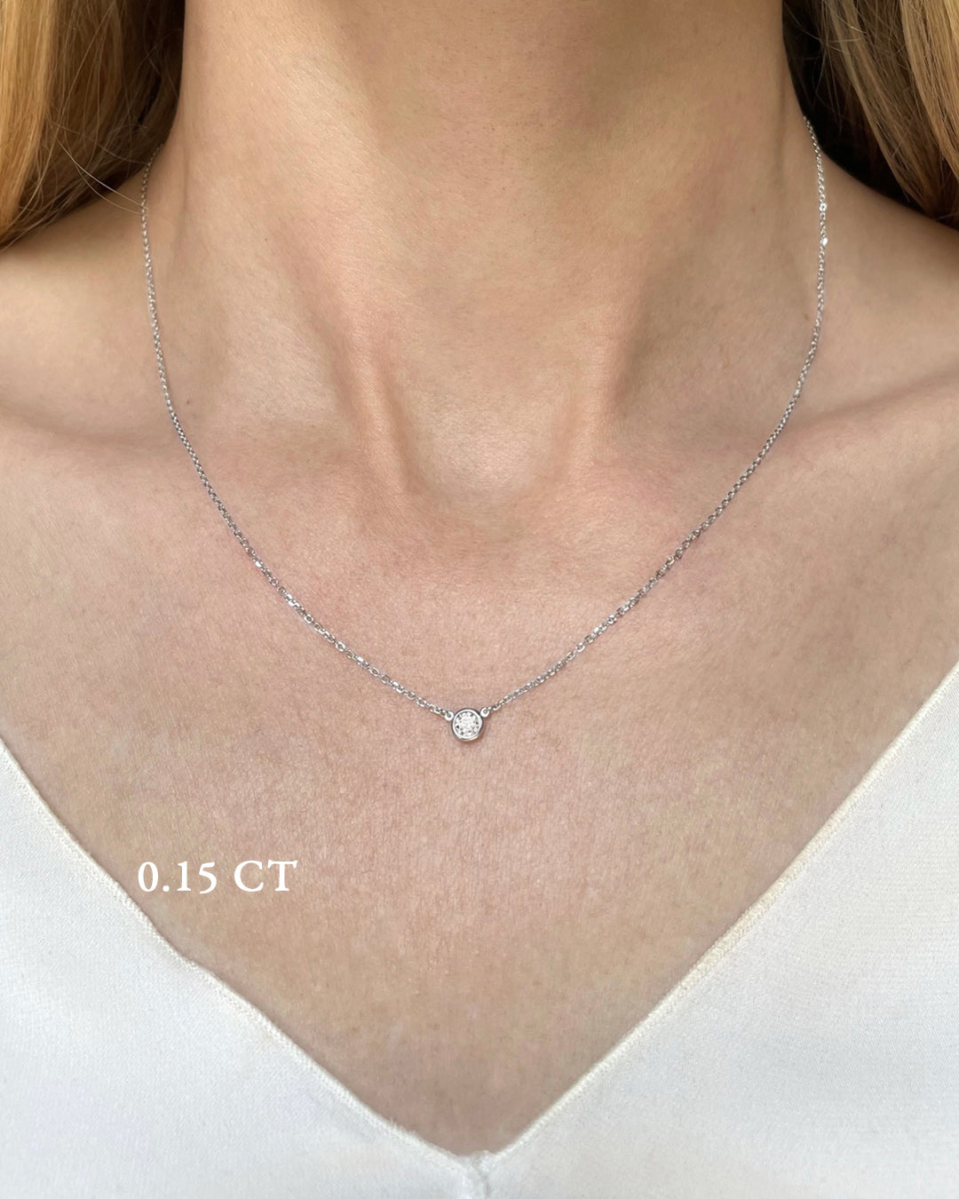 A delicate white gold necklace with a 0.15 carat diamond, bezel set, shown on a model's neck. 