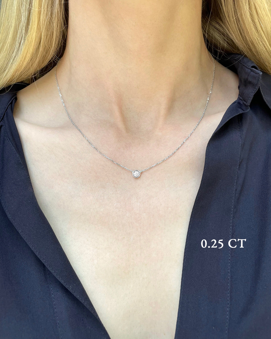 A delicate white gold necklace with a 0.25 carat diamond, bezel set, shown on a model's neck. 