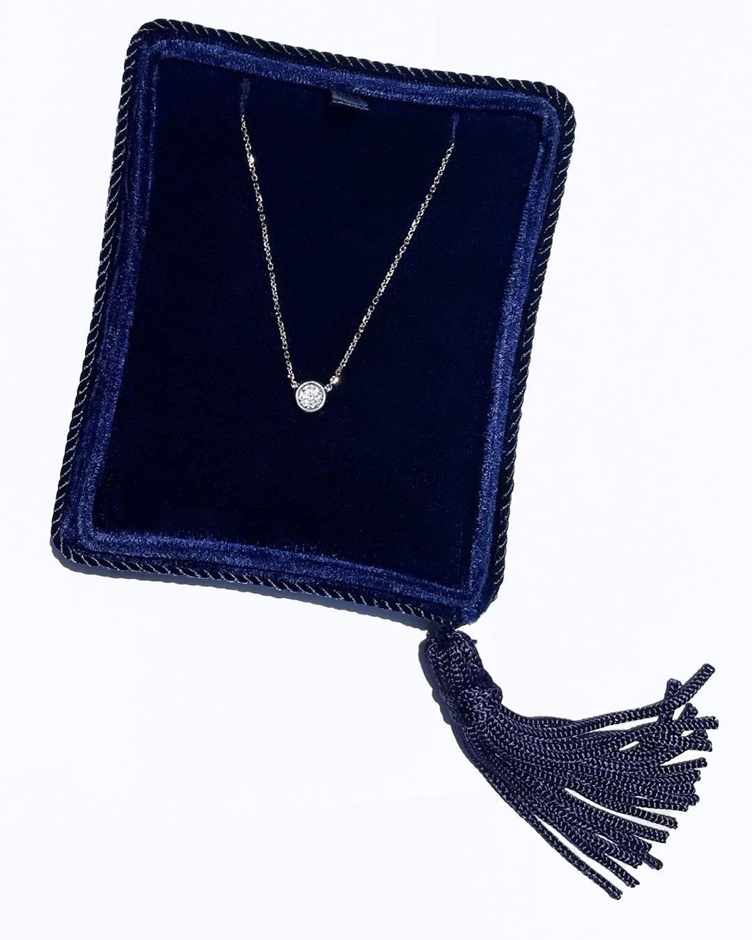 A delicate 14k white gold chain necklace with a 0.40 carat round brilliant-cut diamond bezel set pendant, displayed inside a dark navy velvet jewelry box with a tassel.