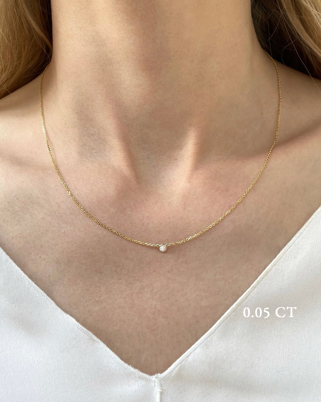 A delicate yellow gold necklace with a 0.05 carat diamond, bezel set, shown on a model's neck. 