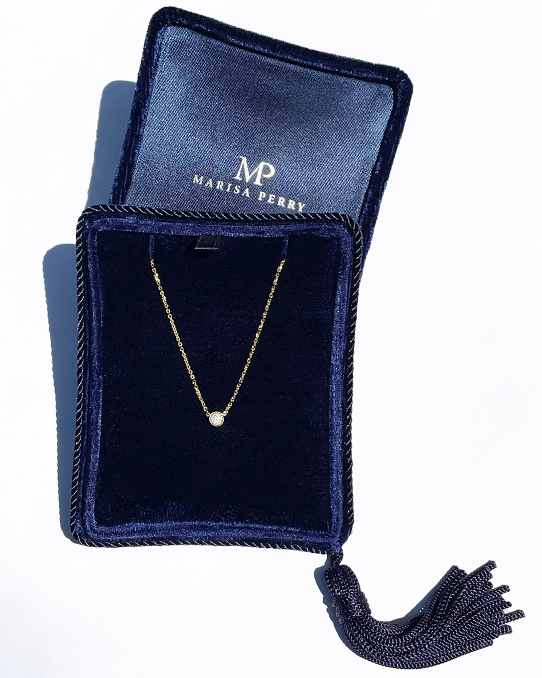 A delicate 14k yellow gold chain necklace with a 0.15 carat round brilliant-cut diamond bezel set pendant, displayed inside a dark navy velvet jewelry box with a tassel.