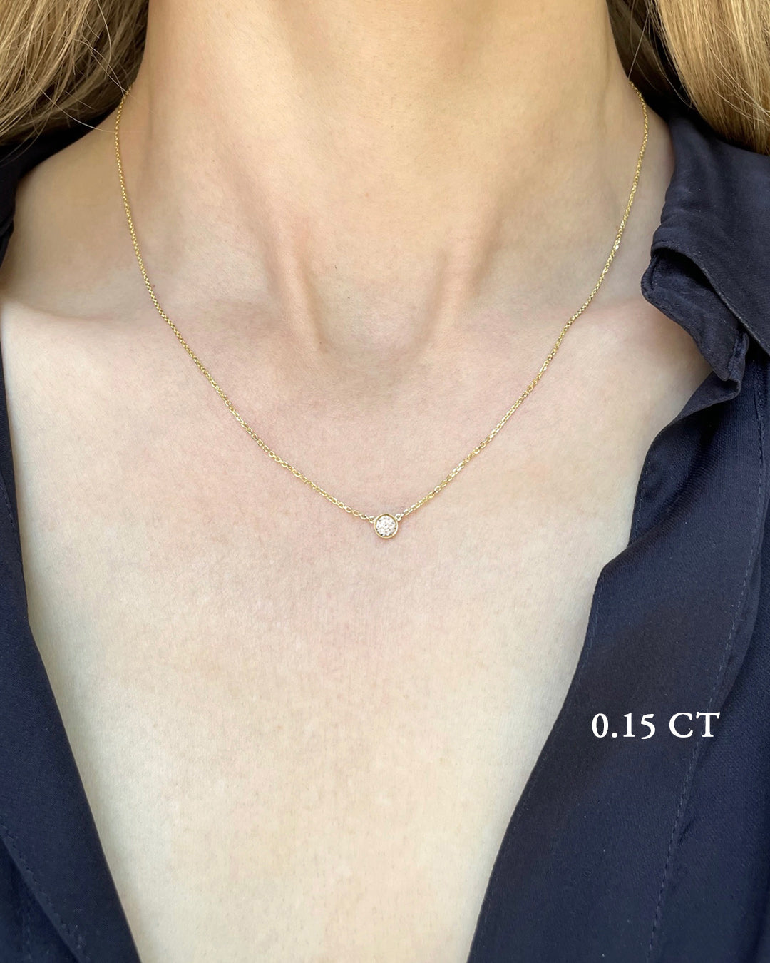 A delicate yellow gold necklace with a 0.15 carat diamond, bezel set, shown on a model's neck. 