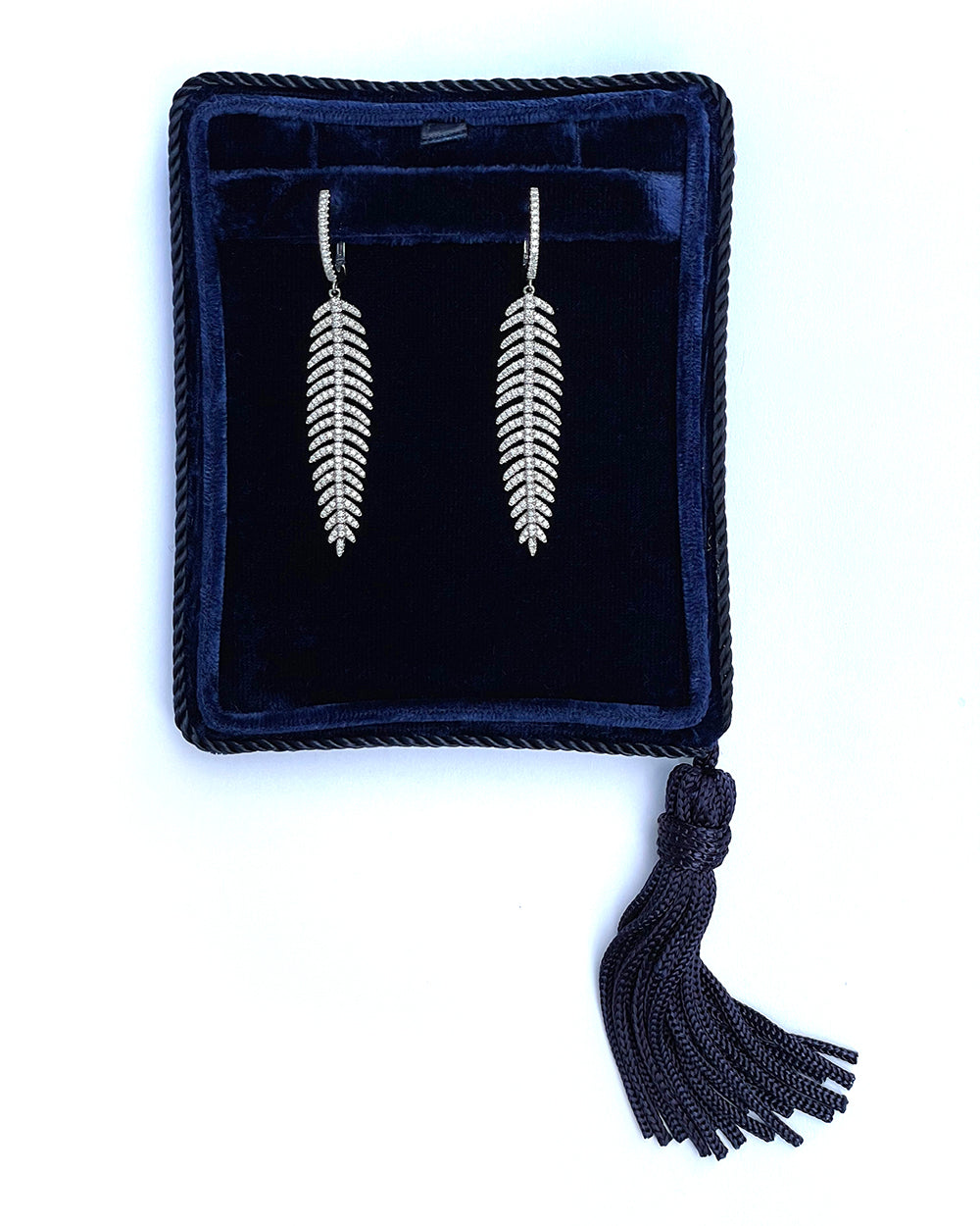 Diamond feather quill earrings in 18K white gold displayed in a navy velvet jewelry box.