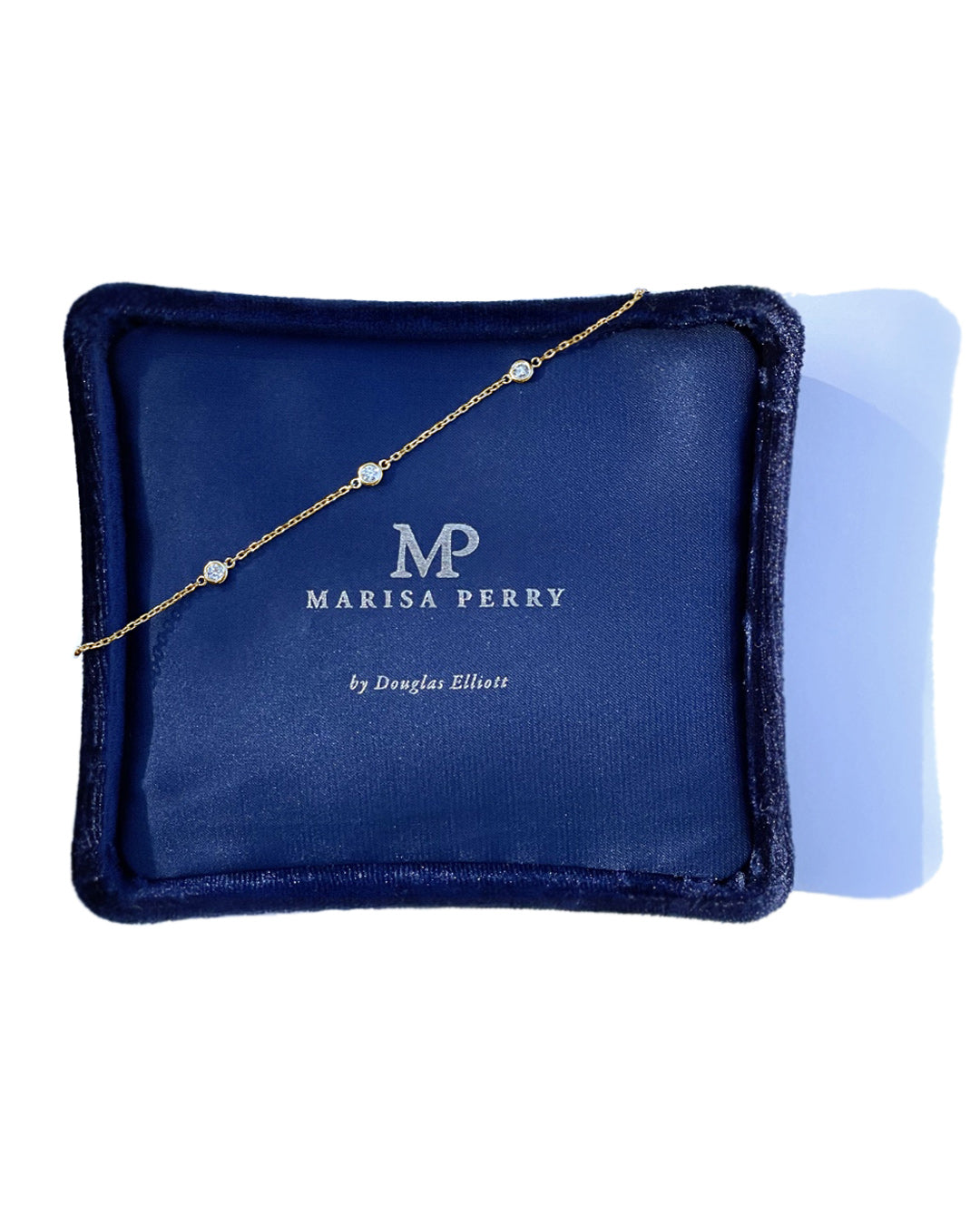 Yellow gold diamond station bracelet displayed across a navy Marisa Perry jewelry box, featuring bezel-set round diamonds.