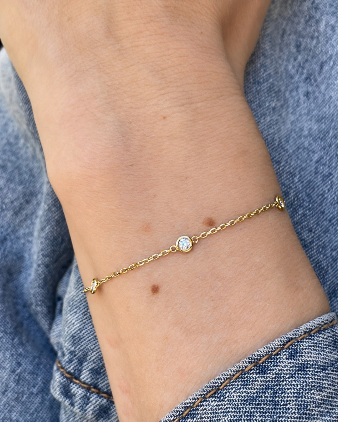 Bezel Set Diamond Station Bracelet in 14K yellow gold worn on a wrist, highlighting its delicate chain and diamond accents.