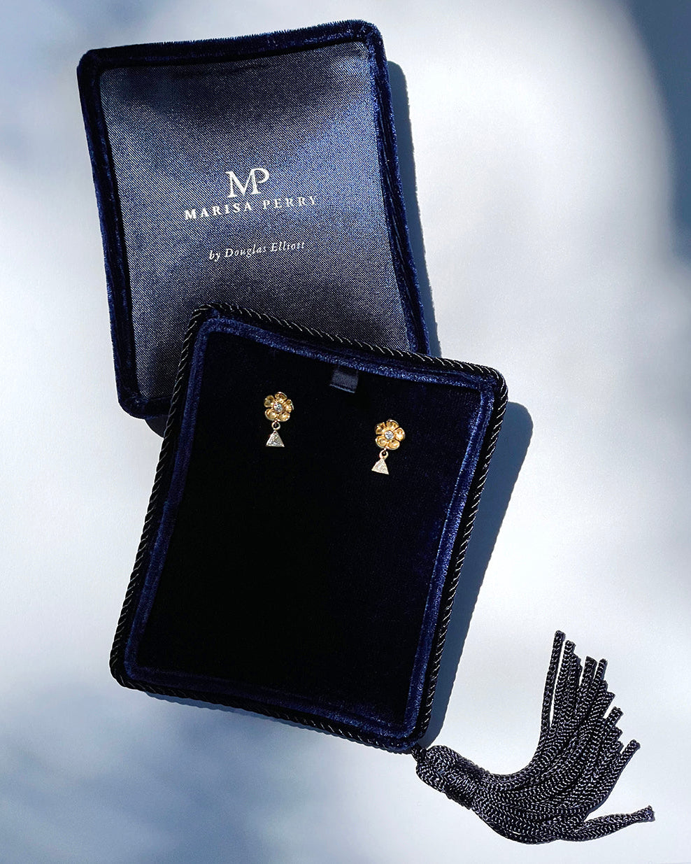 Pair of gold earrings in a Marisa Perry jewelry box on a light gray background