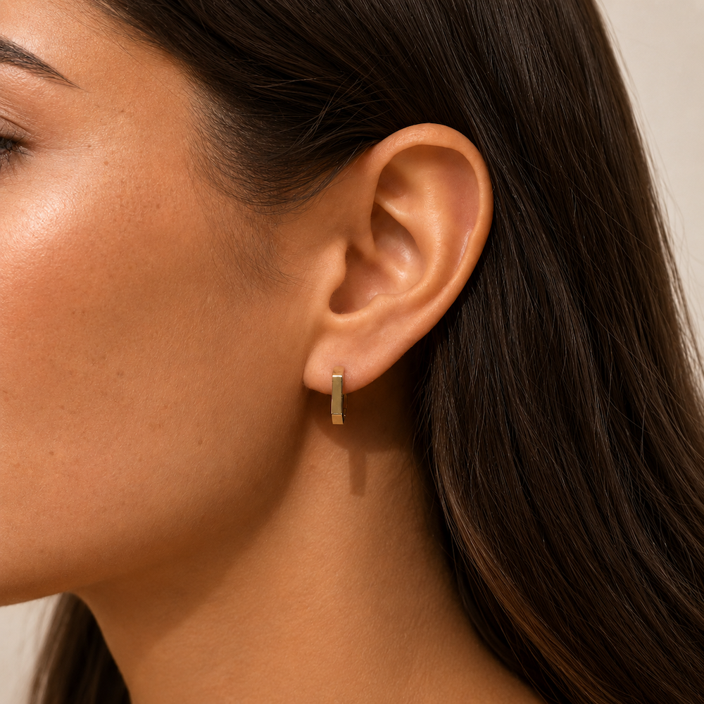 Close-up of a model wearing yellow gold heptagon huggie hoop earrings.