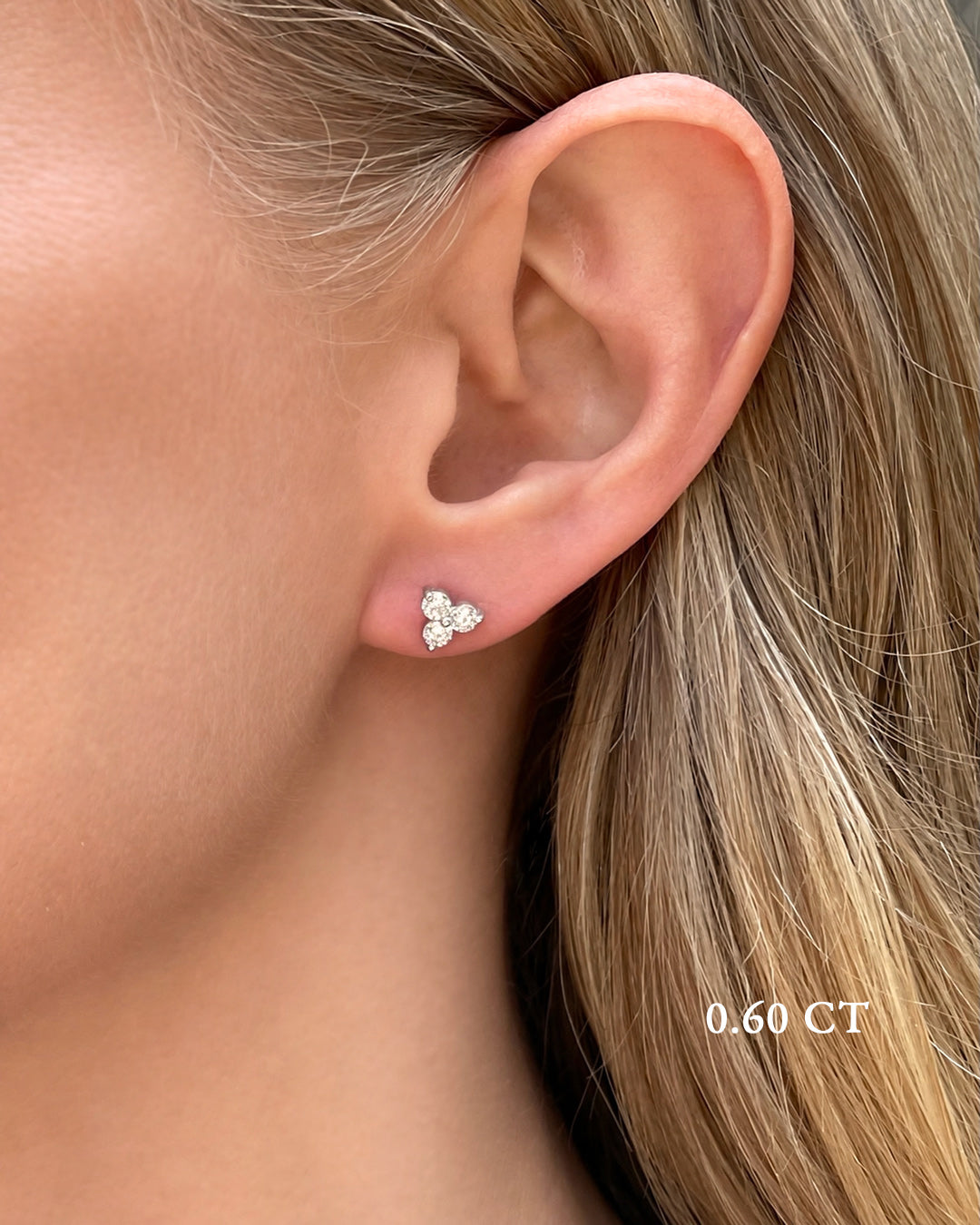 A close-up of a model wearing medium diamond trilogy stud earrings in 14K white gold featuring 0.60 TCW of round brilliant-cut diamonds.