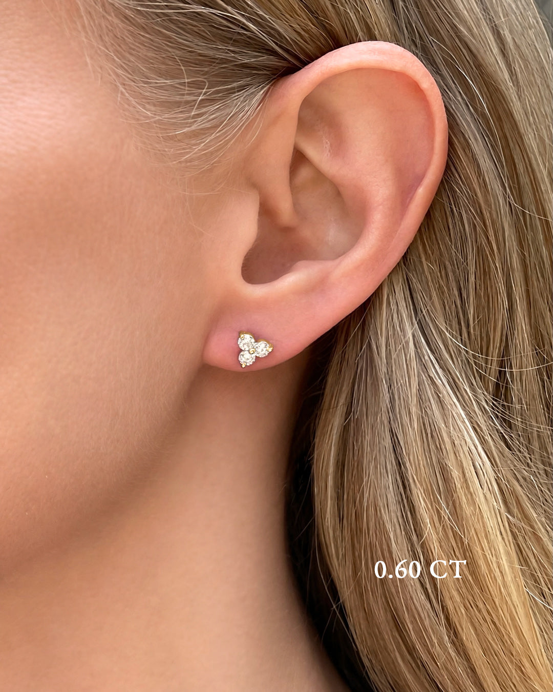 A close-up of a model wearing medium diamond trilogy stud earrings in 14K yellow gold featuring 0.60 TCW of round brilliant-cut diamonds.