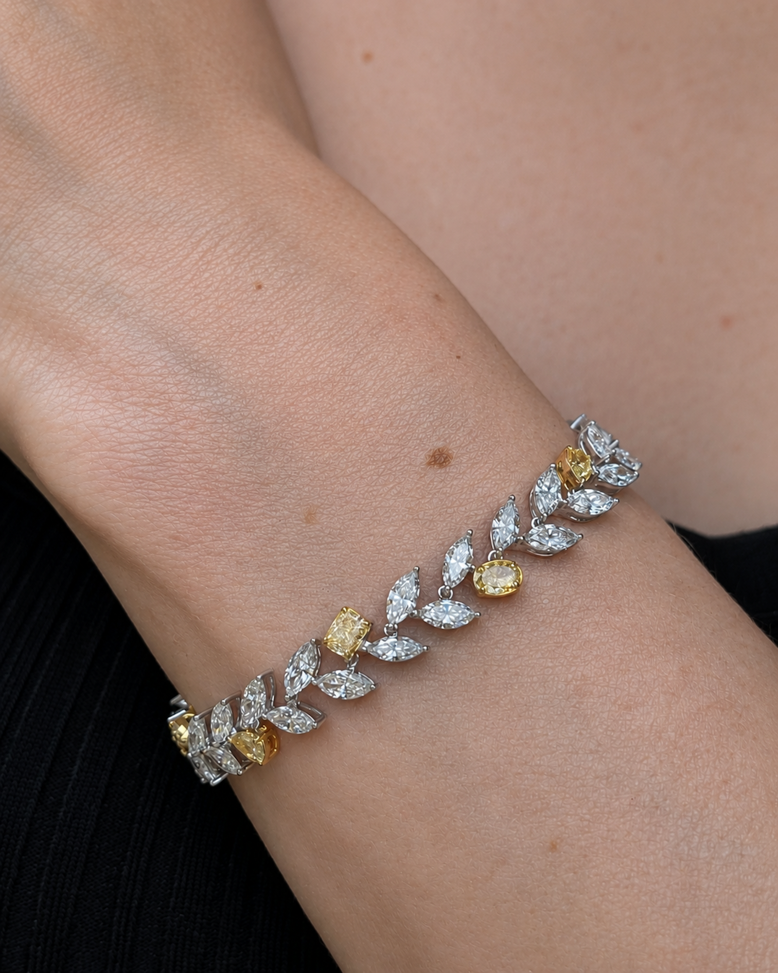 A close-up of a model wearing a mixed shape white and yellow diamond bracelet in 18K white and yellow gold.