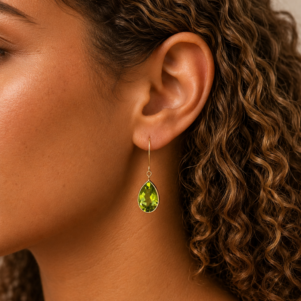 Close-up of a model with curly hair wearing green pear shape peridot drop earrings.