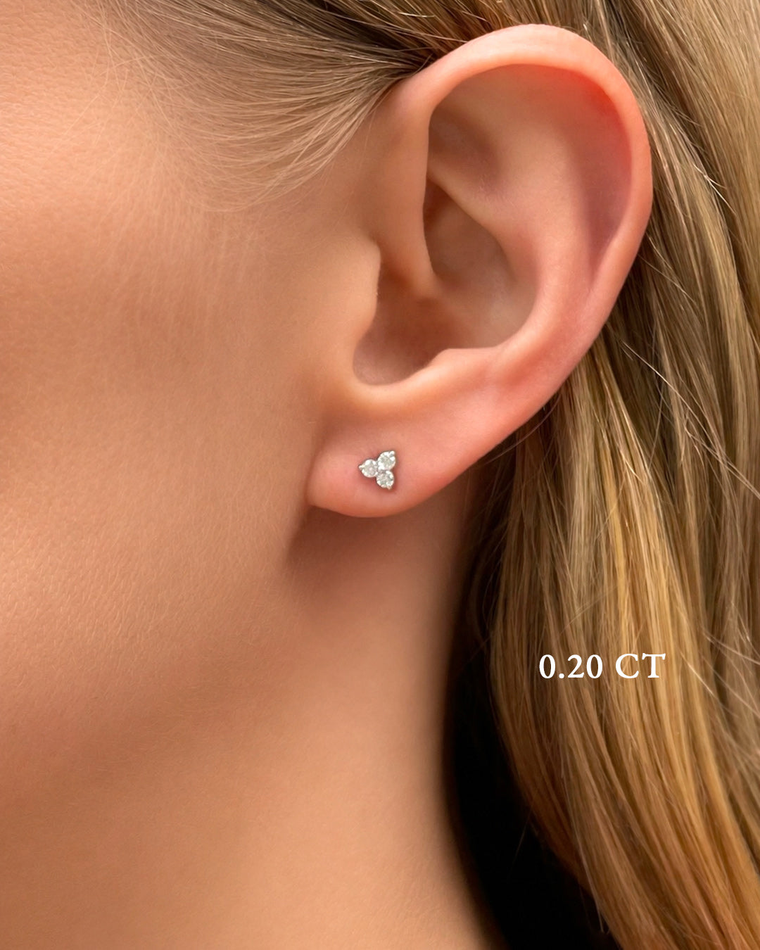 Close-up of a model wearing petite trilogy diamond stud earrings in white gold.