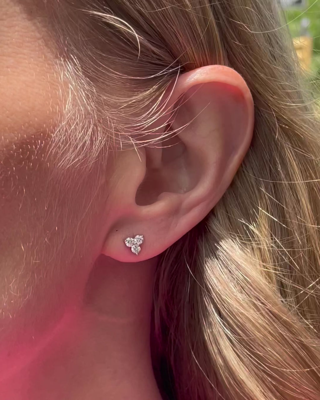 A model moving slowly, showing angles of small diamond trilogy stud earrings in 14k white gold.