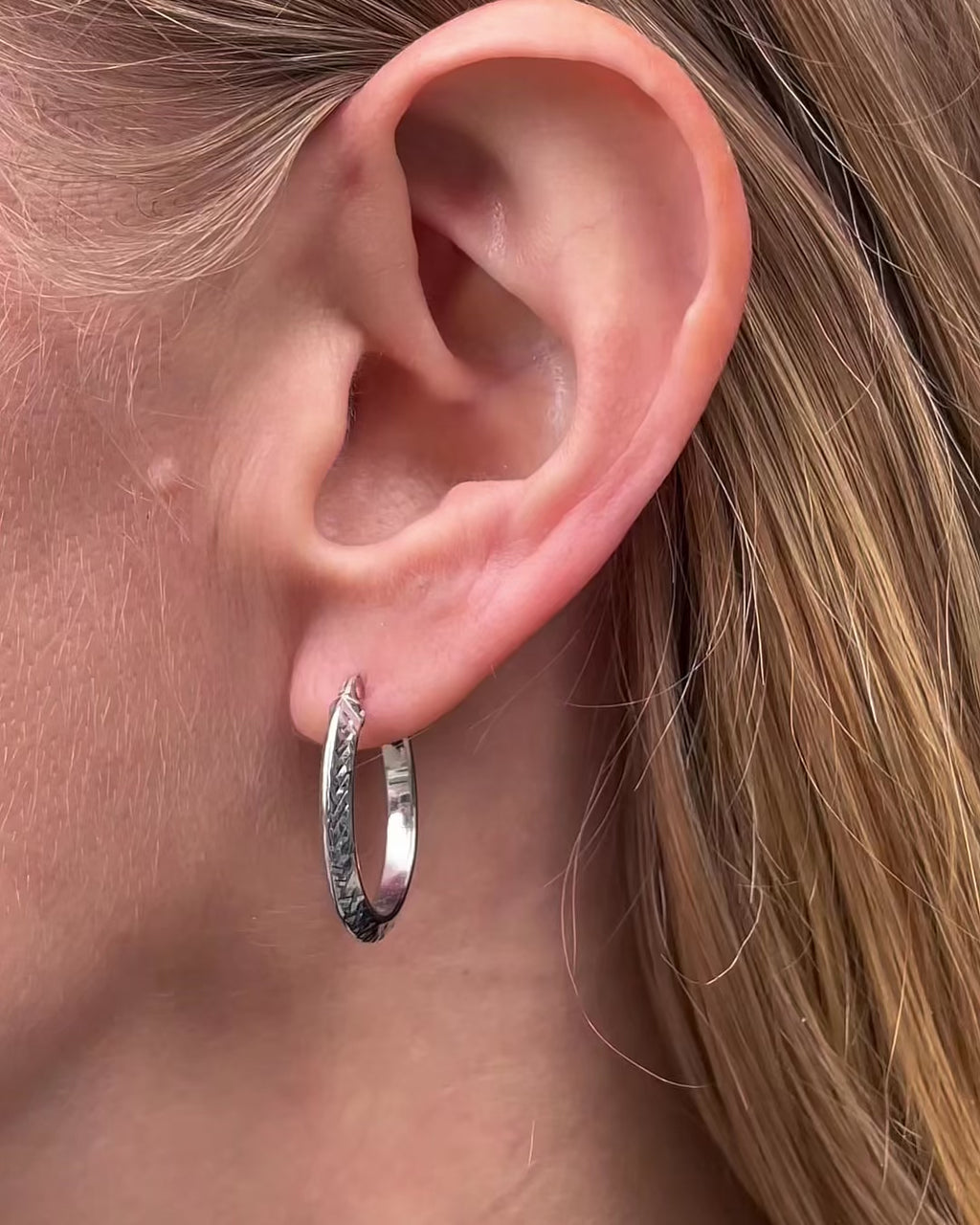 Video of knife edge oval hoop earrings in white gold worn by a model, showcasing their diamond-cut finish and oval silhouette.