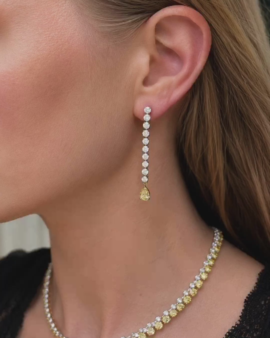 Fancy yellow pear diamond drop earrings in white gold worn by a model, shown with close-up views of the earrings, hand-held details, and in luxury navy jewelry box.