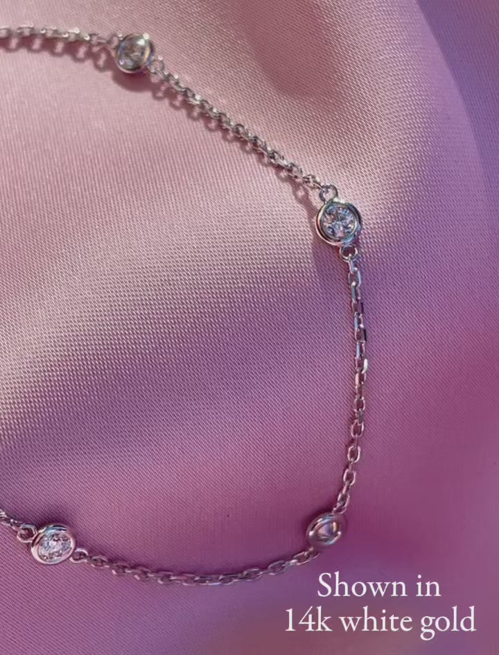 Bezel Set Diamond Station Bracelet ,shown in 14K white gold. Displayed on pink fabric, highlighting the round diamonds, delicate chain and lobster clasp.