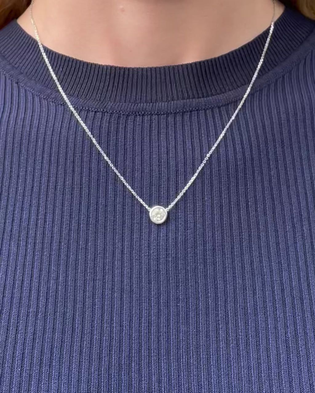 A model moving slowly, from far to close-up, showing details of the 0.75 ct bezel set diamond pendant necklace in 14k white gold.