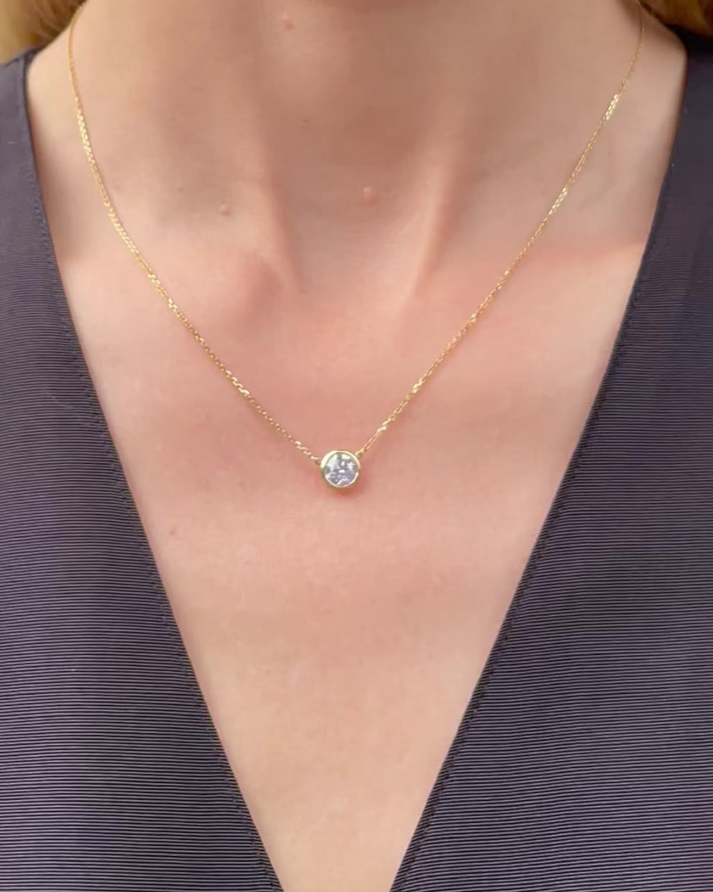 A model moving slowly, from far to close-up, showing details of the 0.75 ct bezel set diamond pendant necklace in 14k yellow gold.