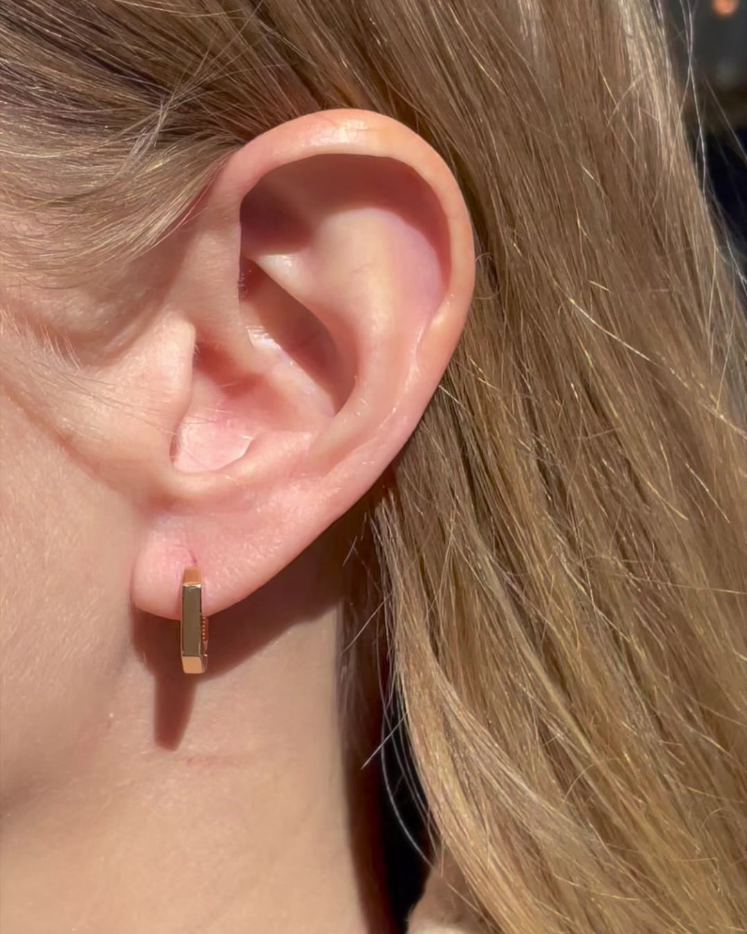 Model moving slowly, showing different angles of heptagon huggie hoop earrings.