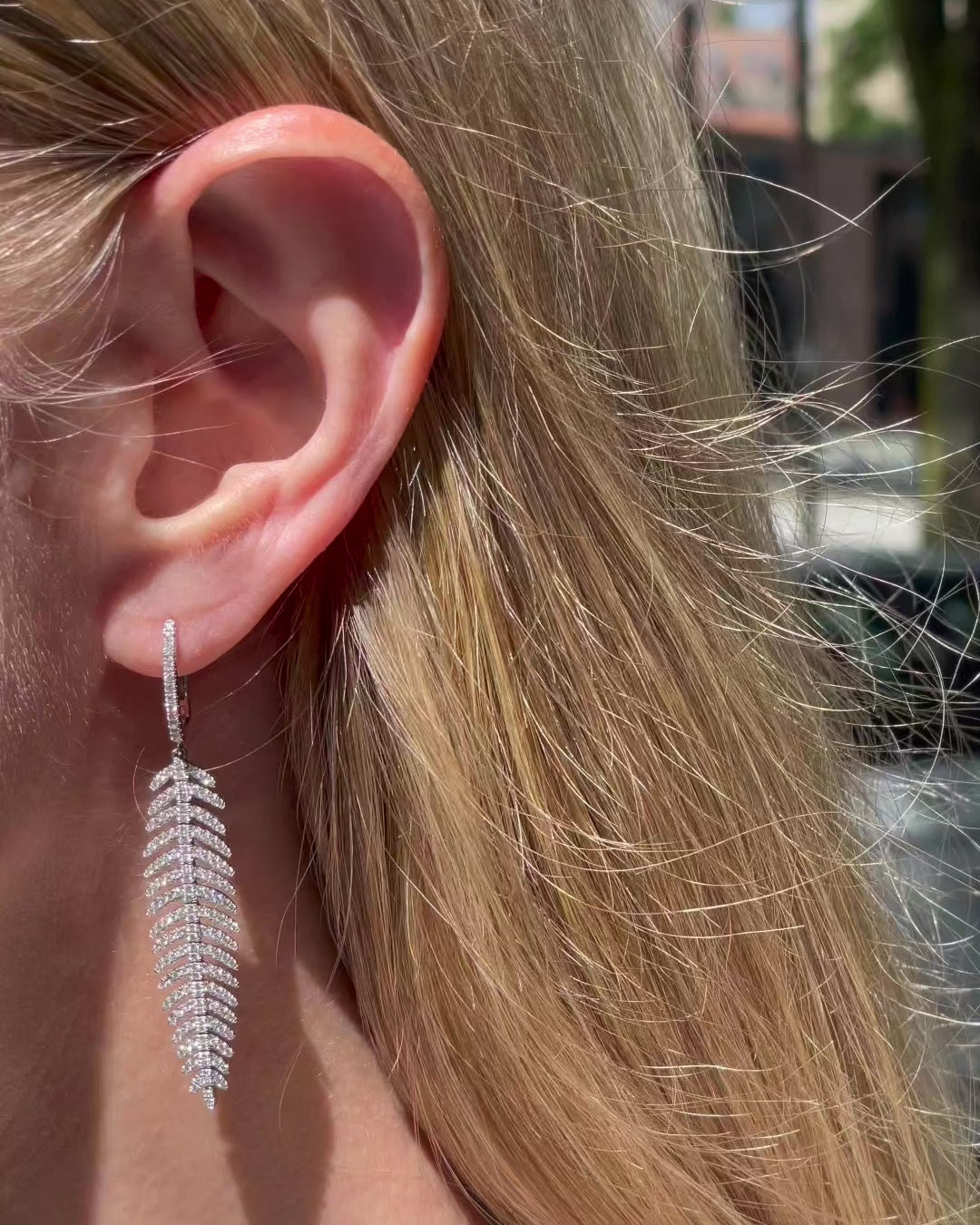 Model wearing diamond feather quill earrings in 14k white gold, moving slowly as they catch the light.