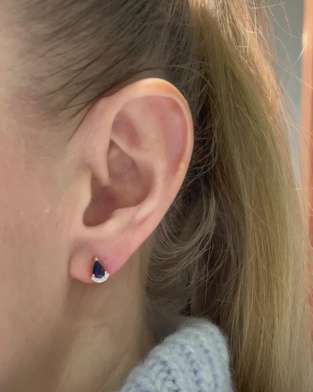 model moving slow wearing pear shaped blue sapphire and diamond stud earrings.