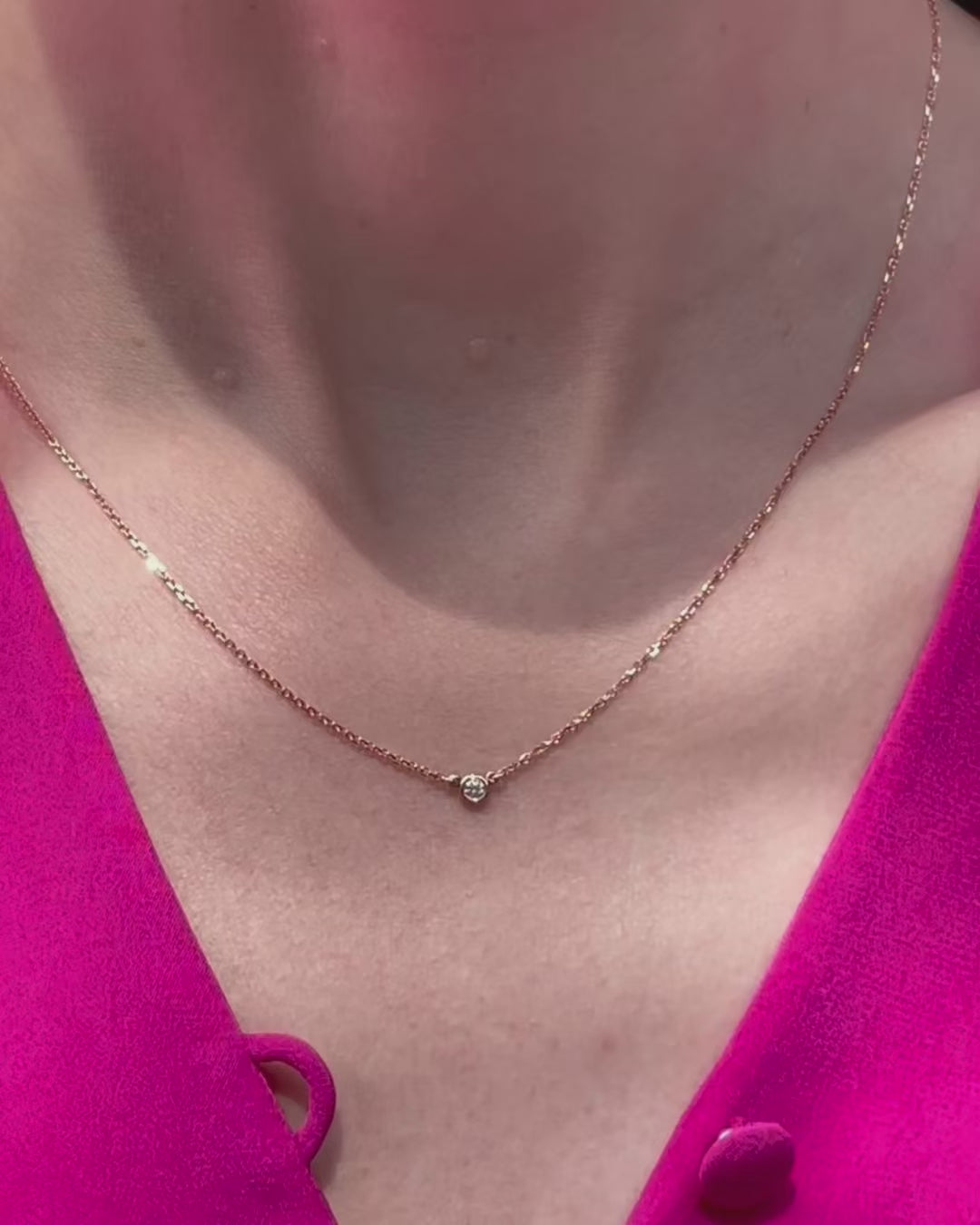A model moving slowly, from far to close-up, showing details of the 0.05 ct bezel set diamond pendant necklace in 14k rose gold.