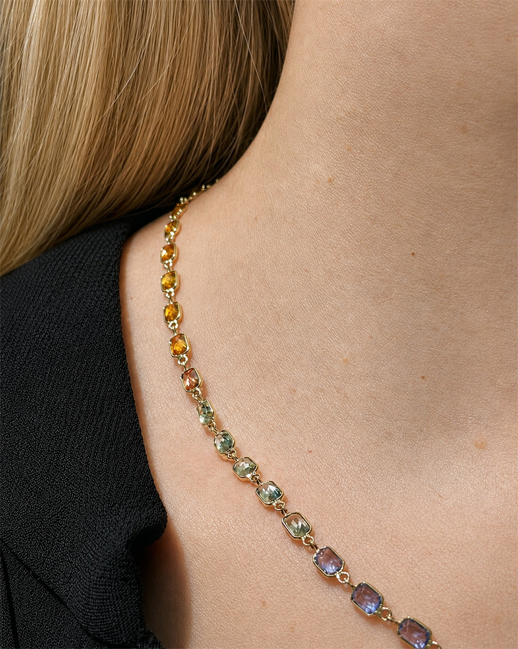 Close up details of a rainbow sapphire bezel set necklace with natural multicolor sapphires set in yellow gold.