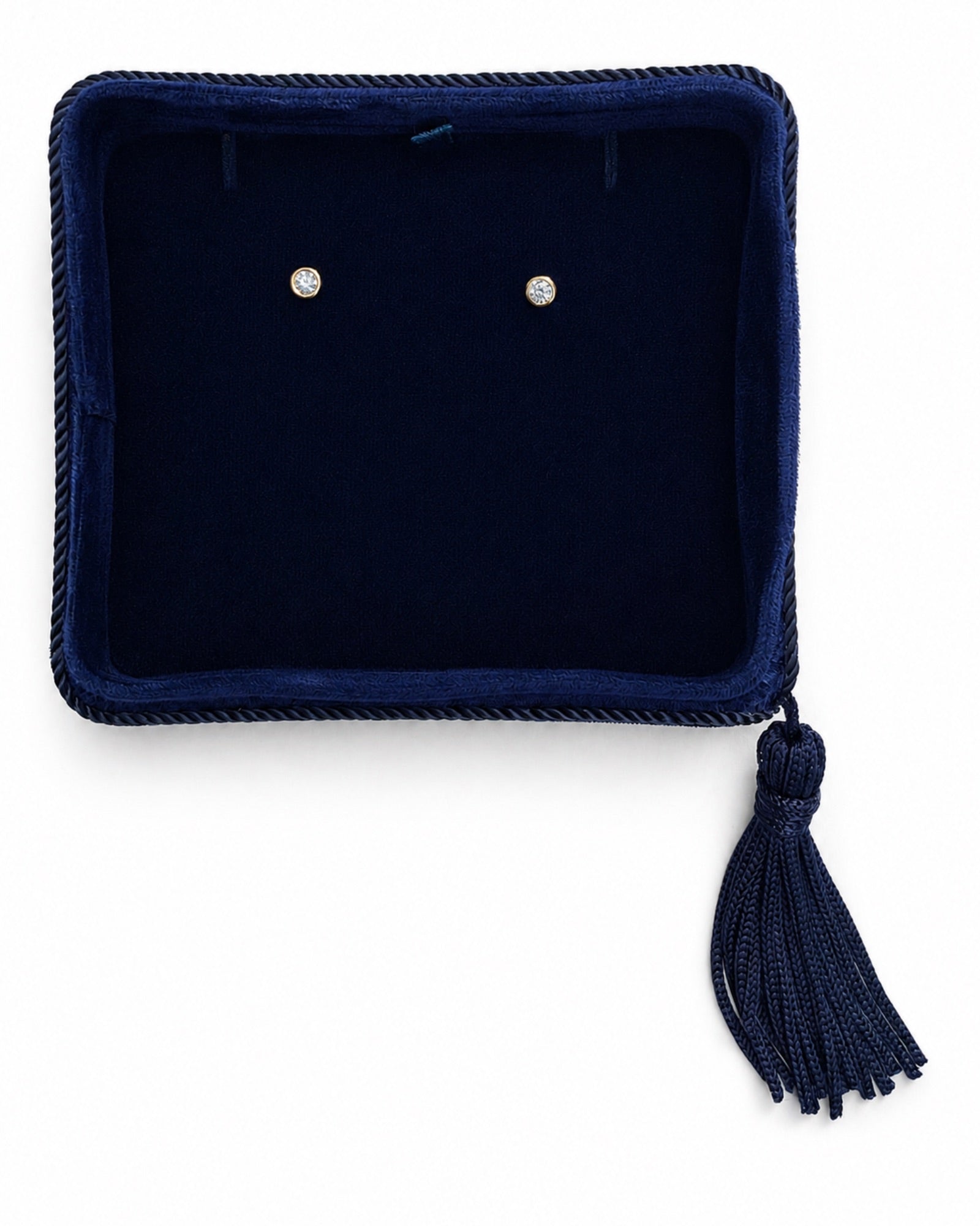 A pair of small round bezel set diamond stud earrings displayed on a dark navy blue velvet jewelry box.