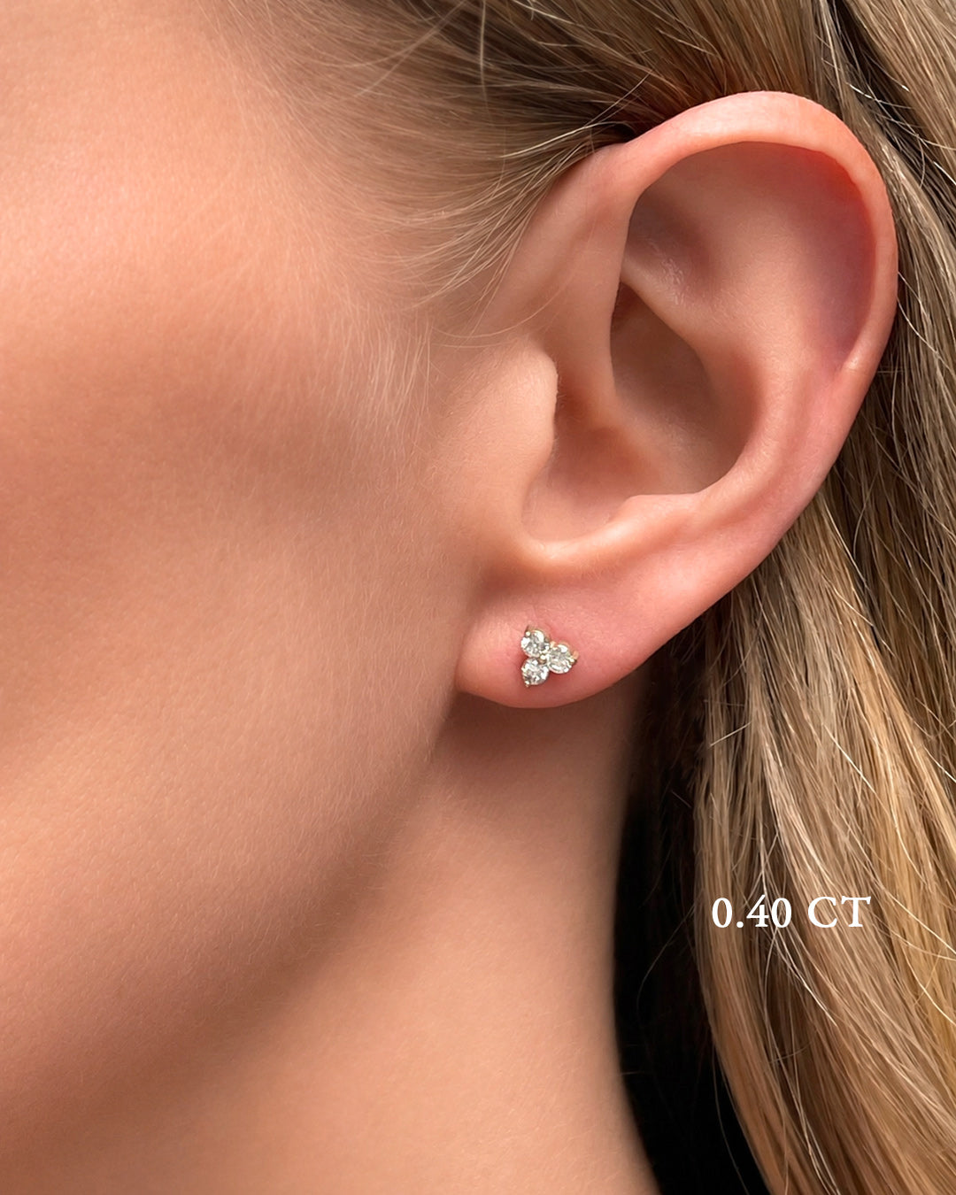 A blonde model wearing small diamond trilogy stud earrings in 14k yellow gold with a total of 0.40 carats of round brilliant-cut diamonds.