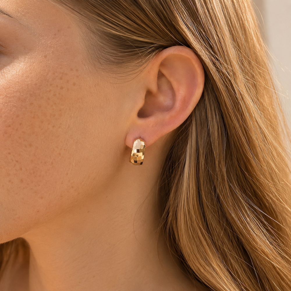 Model wearing yellow gold textured wide huggie hoop earrings.